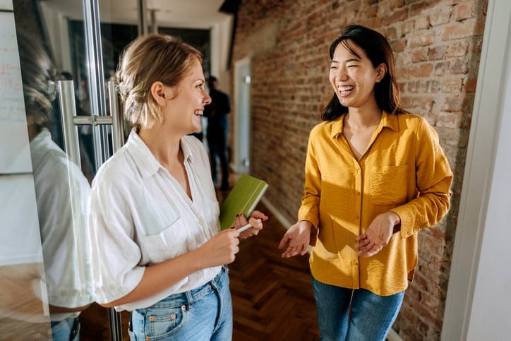 Two female colleagues chatting in hallway.