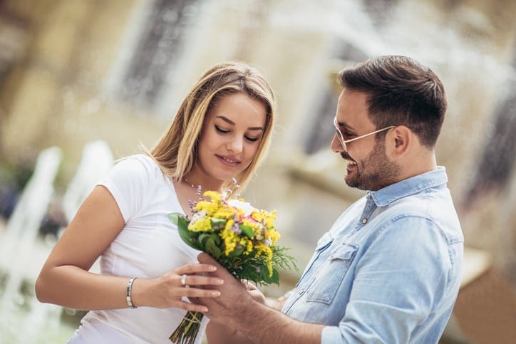 Man surprising woman with flowers.