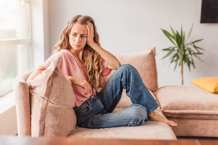 Sad girl sitting on sofa at home and thinking. Young woman suffering from depression feeling sad and lonely