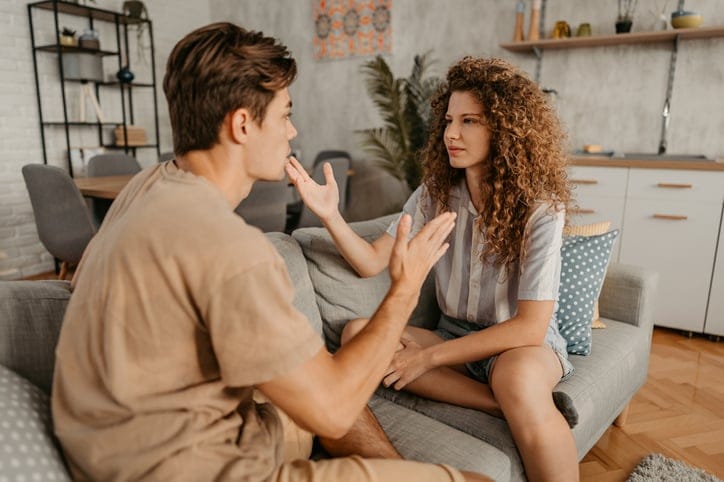 Young couple with relationship problems, sitting on the sofa in the living room and arguing.