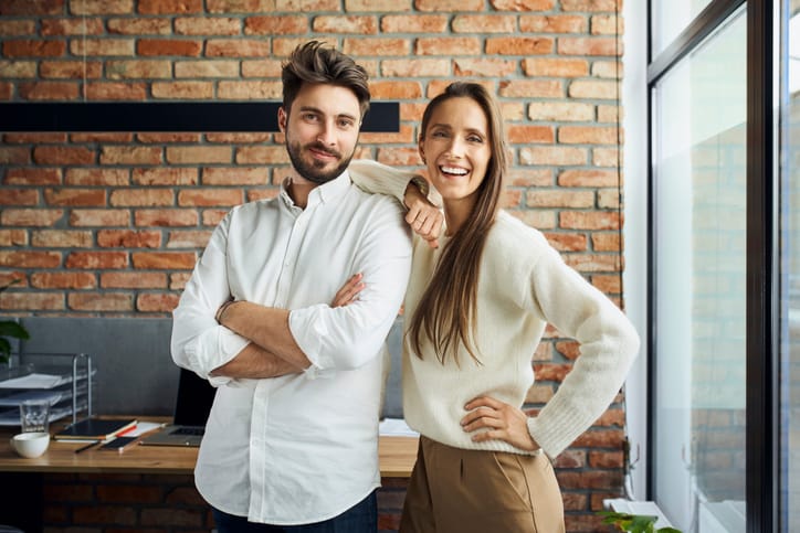 Portrait of successful couple standing at small office. Happy new business partners posing together