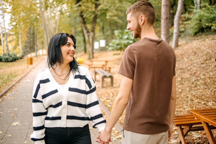 Young couple in love walking in city park on yellow leaves in Autumn