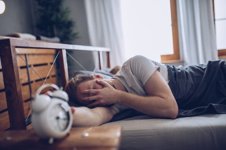 Sleeping man disturbed by alarm clock early in the morning.