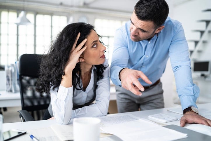 Man standing over his female coworker at her desk.