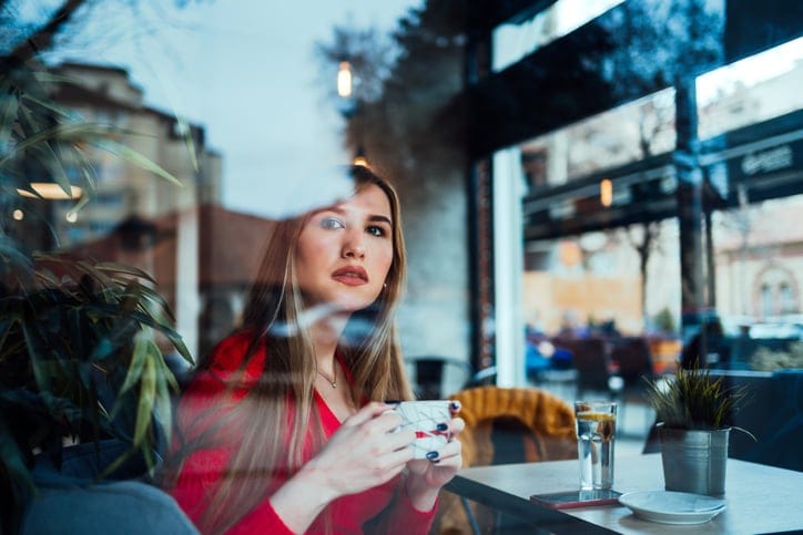 Young caucasian woman drinking coffee in cafe, looking through the window and waits for a friend