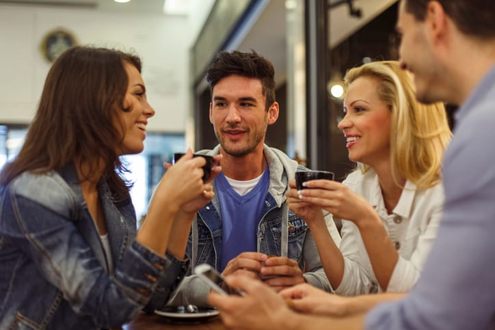 Candid shot of small group of friends sitting together at the table in a coffee shop, chatting and enjoying coffee.