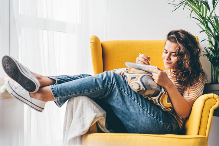 woman writing in notebook on chair