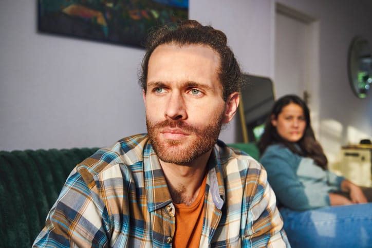 Cropped shot of a handsome young man looking annoyed after arguing with his girlfriend who is sitting in the background