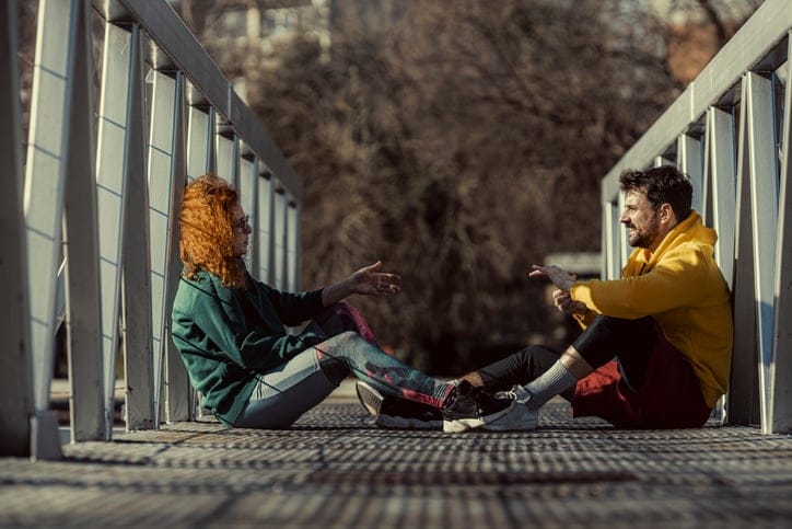 The girl explains to her friend what stretching exercises she wants to do while sitting on the footbridge and resting.