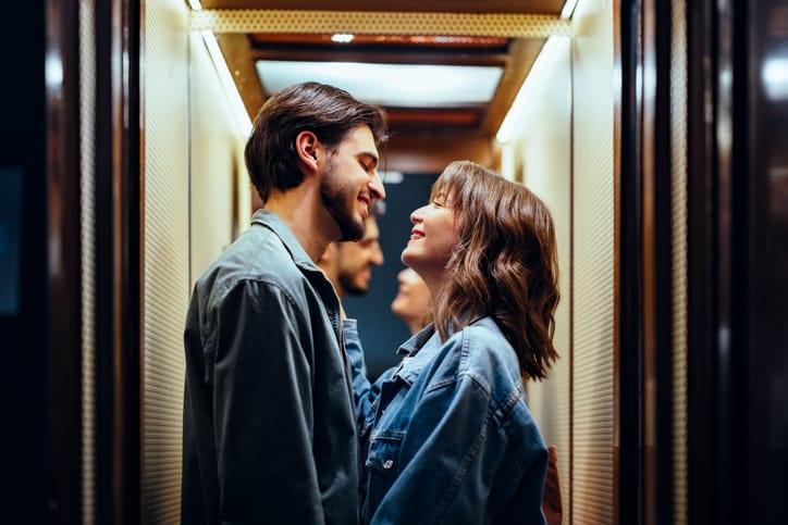 Smiling boyfriend looking at his girlfriend standing together in the elevator.