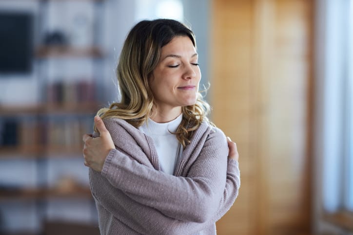 Smiling woman embracing herself at home. Copy space.