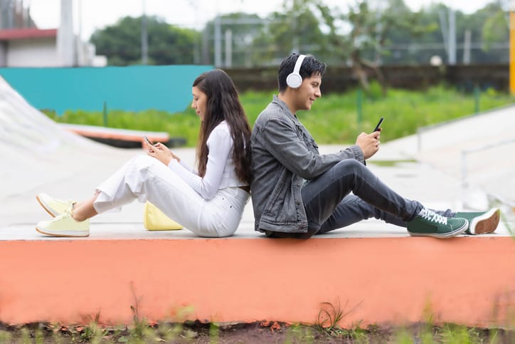 Young woman and young man sitting back to back using their cell phones