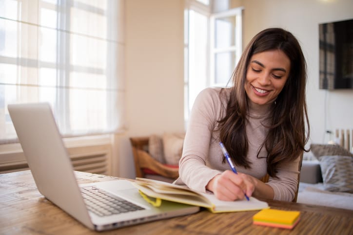 Woman working at computer taking notes.