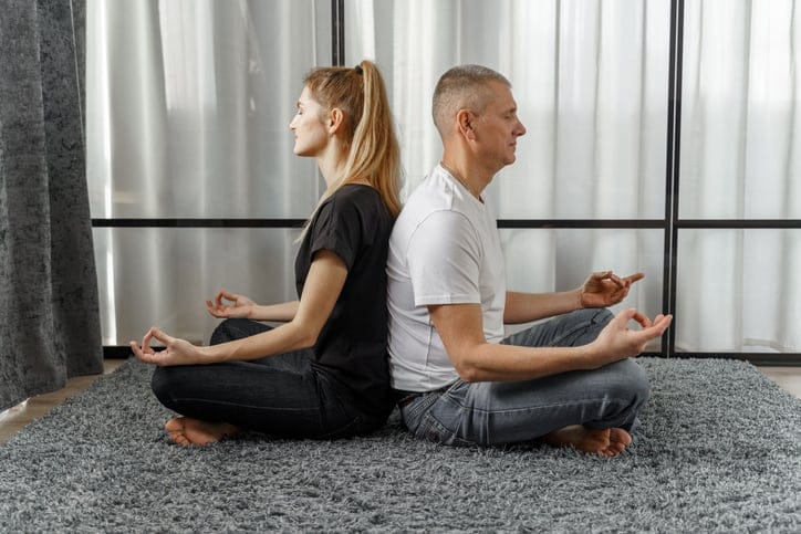 A man and a woman sit back to back doing yoga.