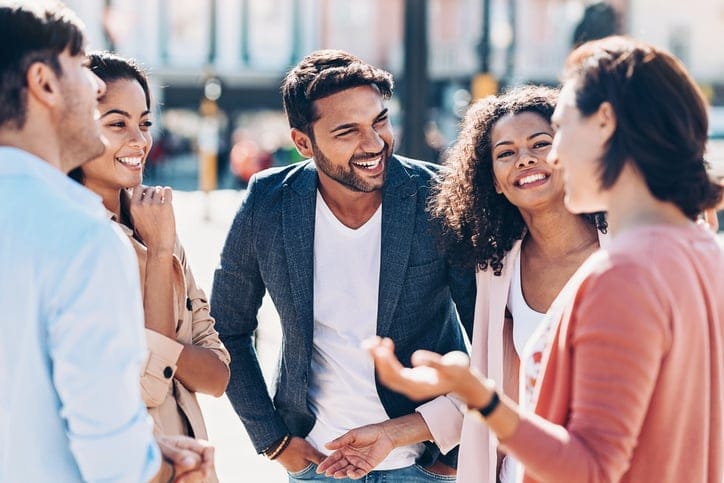 Group of smiling young people talking outdoors.
