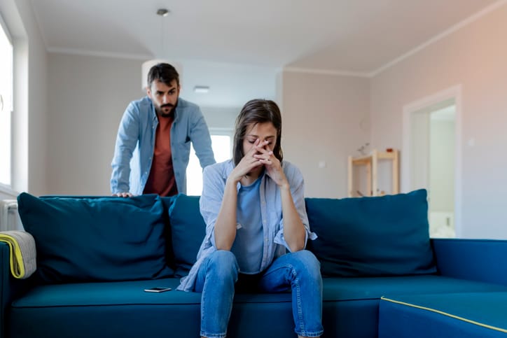 woman with head in hands while boyfriend shouts