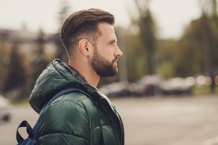 Photo of good mood charming confident young man wear green windbreaker schoolbag walking city street.