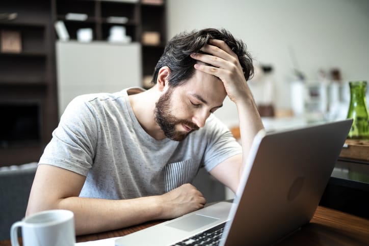 guy looking stressed at desk with laptop
