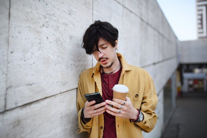 Young man texting outdoors with coffee.