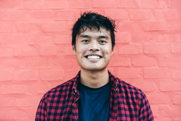 smiling young man in front of pink wall