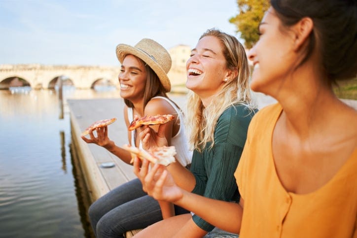 Three beautiful women sitting on the stairs of the city streets eating pizza from a street stall. The happy girls enjoy the weekend together. High quality photo
