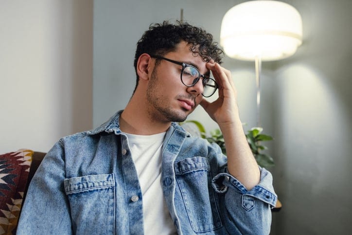 A sad young man in the living room. He suffers from depression