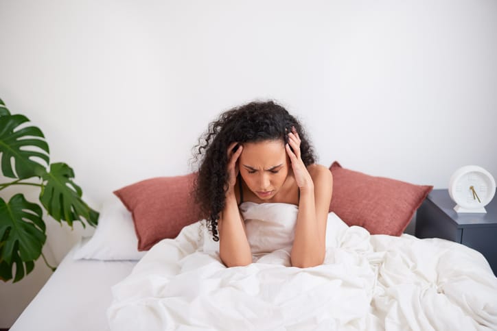 A young multi-ethnic woman sits with head in hands struggling to wake up in bed. High quality photo
