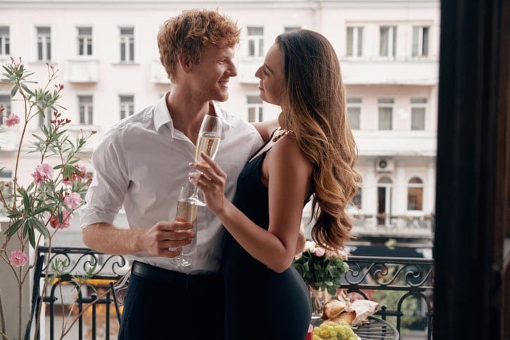Happy young couple embracing while enjoying champagne on the balcony together.