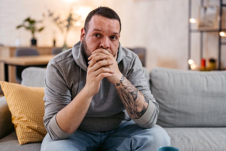 Hopeless young man sitting alone and thinking about problems, covering his mouth.