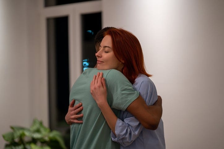 Young multiracial couple woman and man hugging while making up at home, loving supportive wife embracing husband gently, showing love and support. Understanding in relationships, tactility and hugs