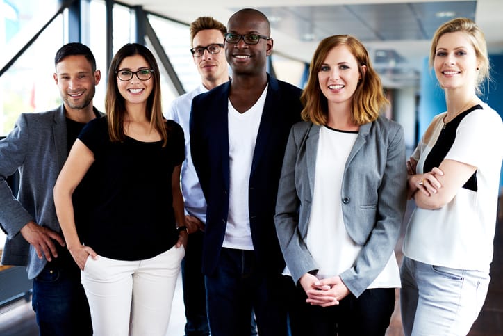 Group of young executives standing, smiling at camera and posing for picture