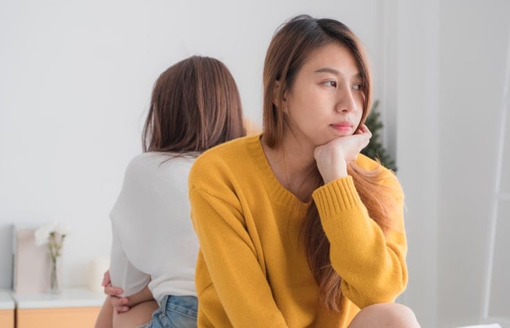 Two female friends sitting back to back.