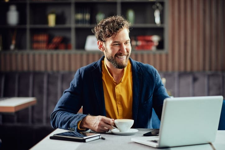 Man drinking coffee and looking at laptop.