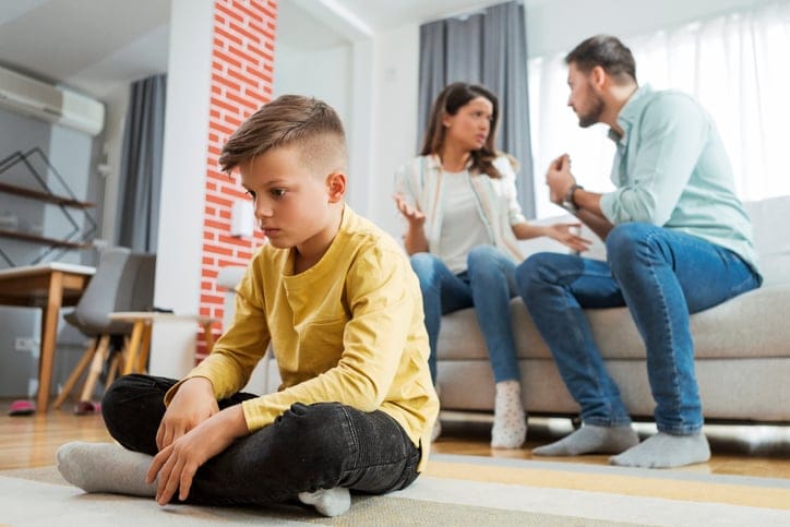 upset kid with parents fighting behind him