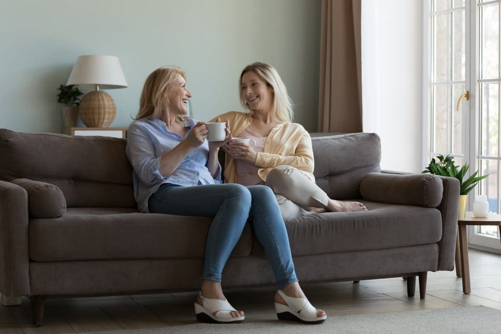 Mother and daughter, chatting and drinking tea on sofa.