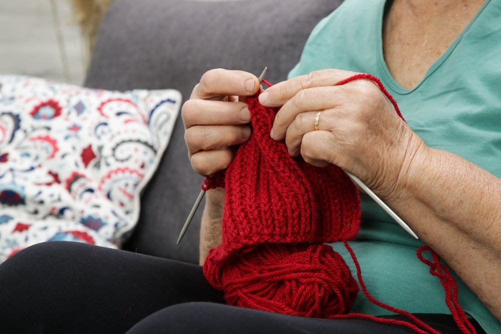 A woman sitting on the couch enjoying knitting.