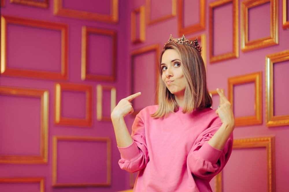 Woman wearing a crown pointing to herself.