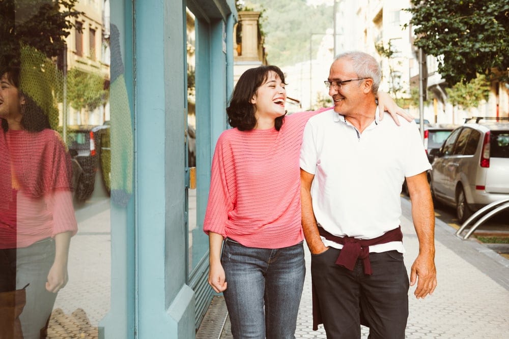 A young woman with her arm around her middle-age father as they laugh and stroll together.