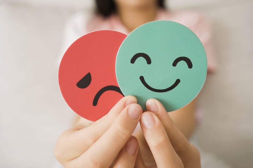 Hands holding a smiling face and a sad face.