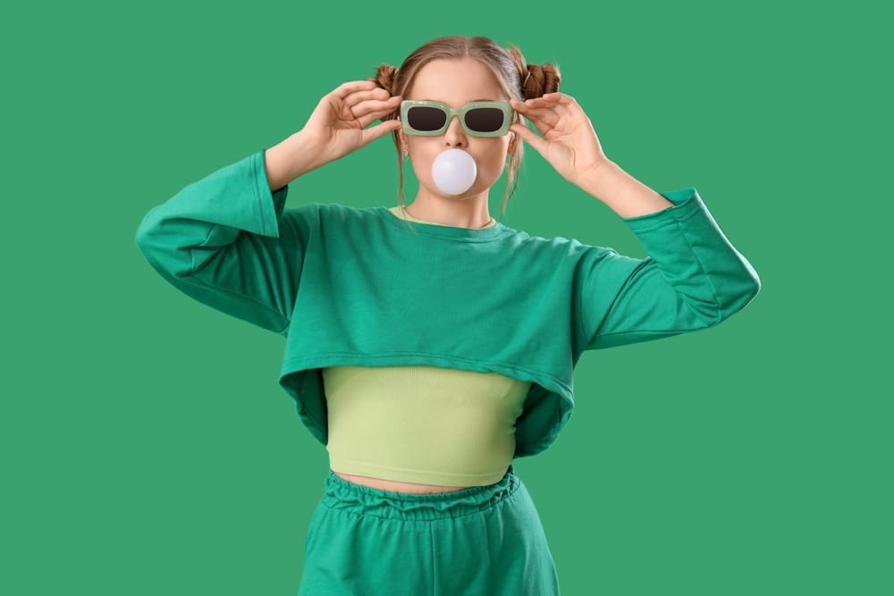 Young Gen Z woman wearing all green chewing bubble gum.