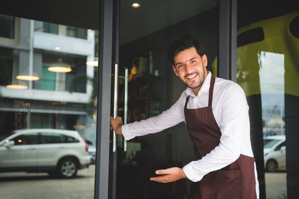 Shop owner holding open the door to customers.