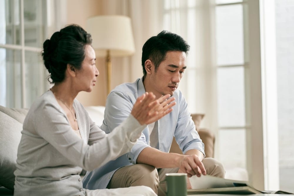 Senior,Asian,Mother,And,Adult,Son,Sitting,On,Couch,In
