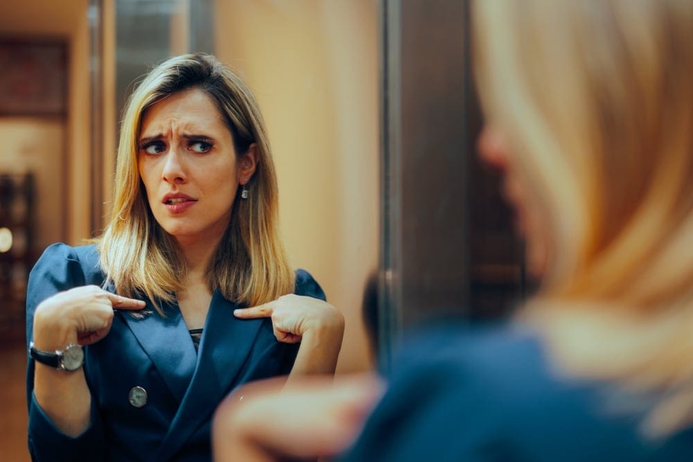 Woman looking in the mirror and insecure.