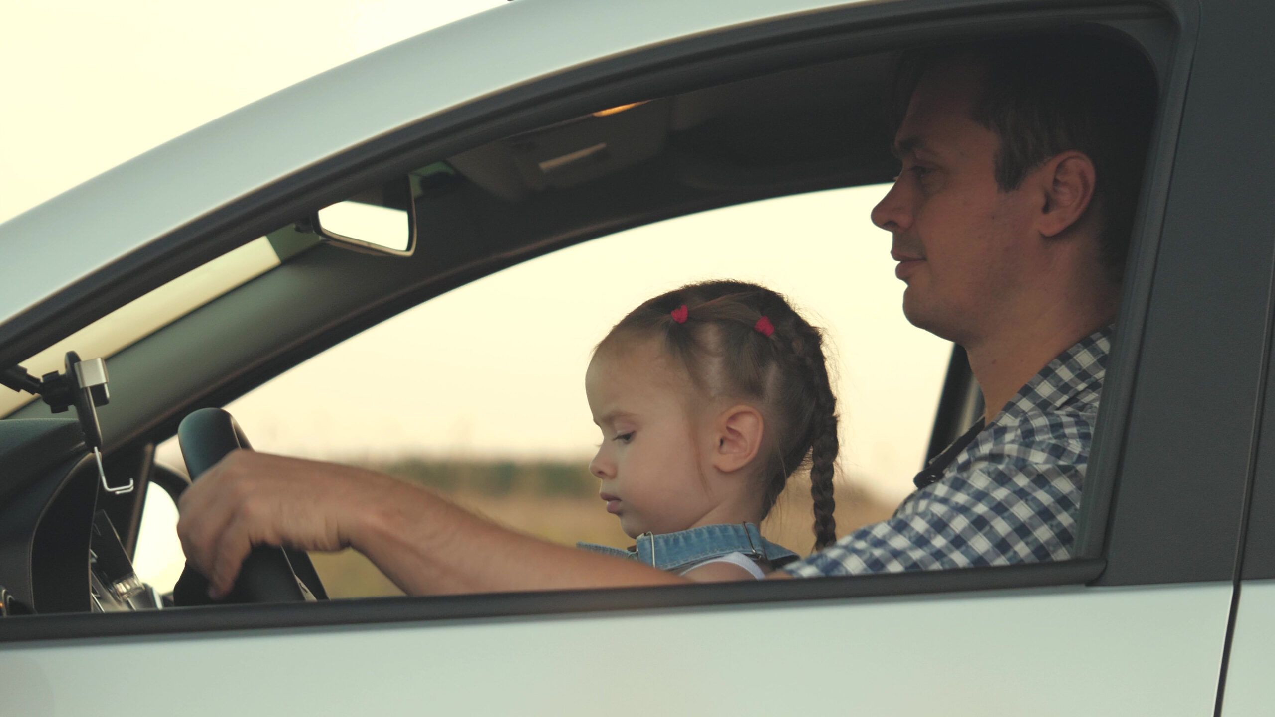 Dad with his daughter at the wheel of car.