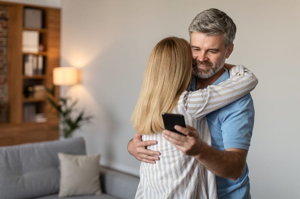 Man looking at his phone over his wife's shoulder.