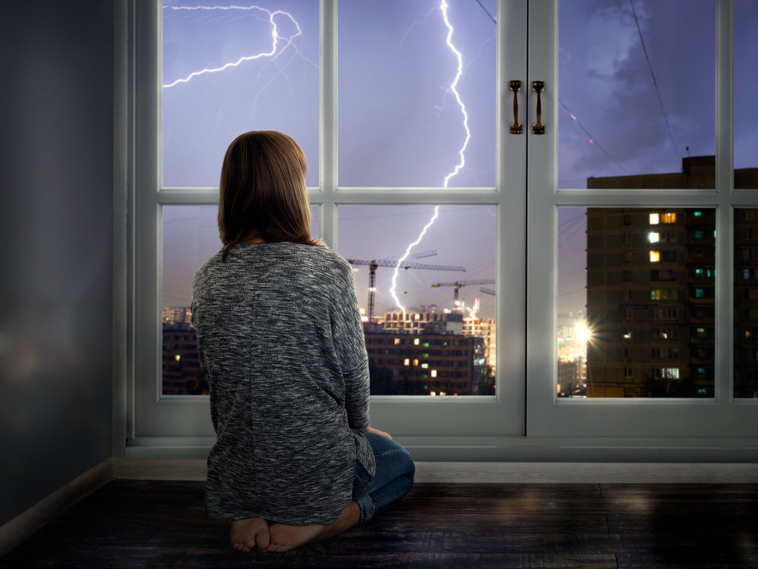 Girl looking outside at a lightning storm.