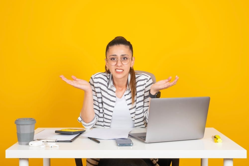Woman shrugging while sitting at her desk.
