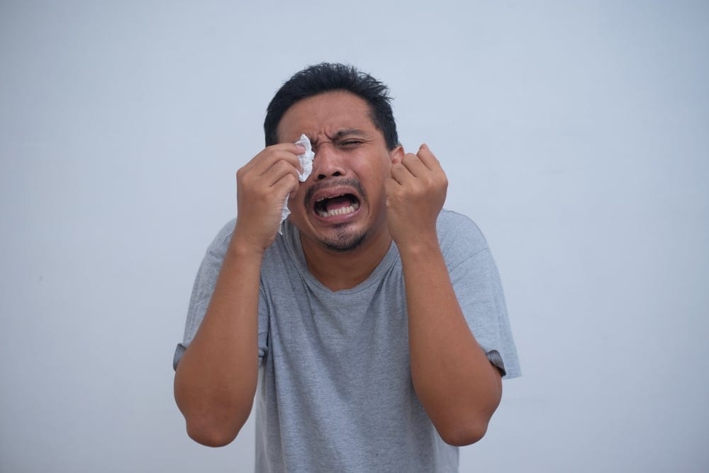 A man crying with a tissue at his eyes.