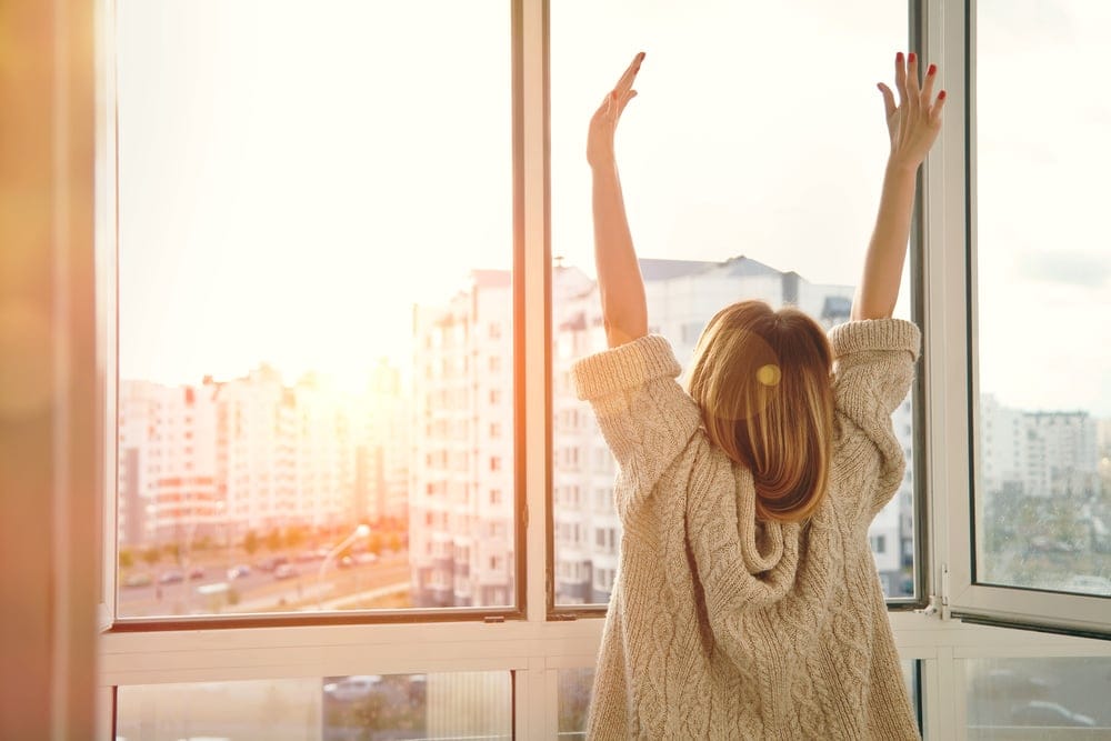 Woman watching the sunrise through her windows.