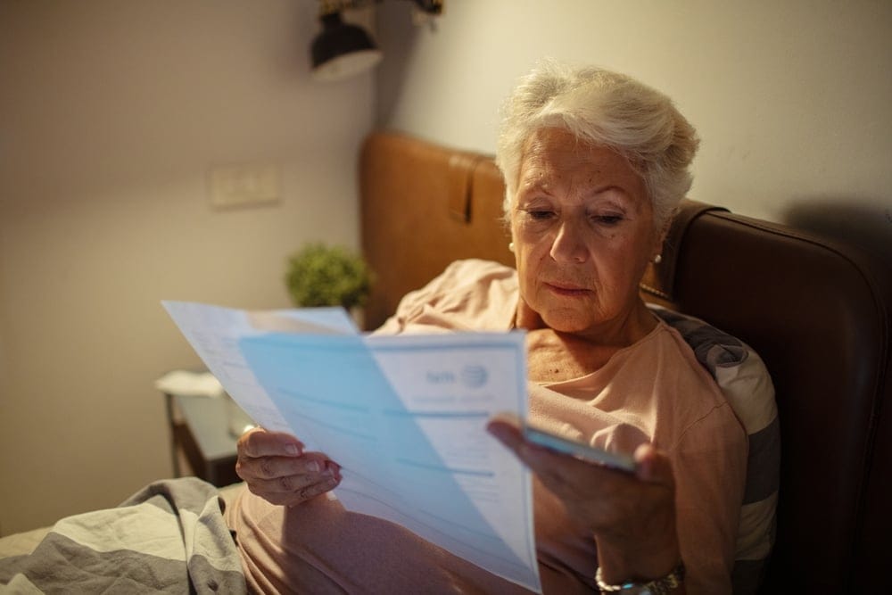 Worried senior woman reading bills in bed at night